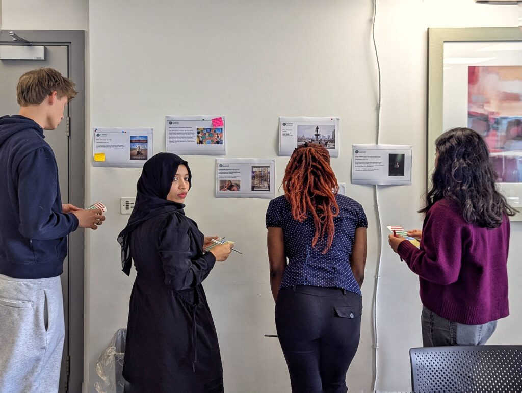 Fleming Centre - Youth panel consultation session, 4 young people stand before a wall looking at sheets of paper which are pinned up .
